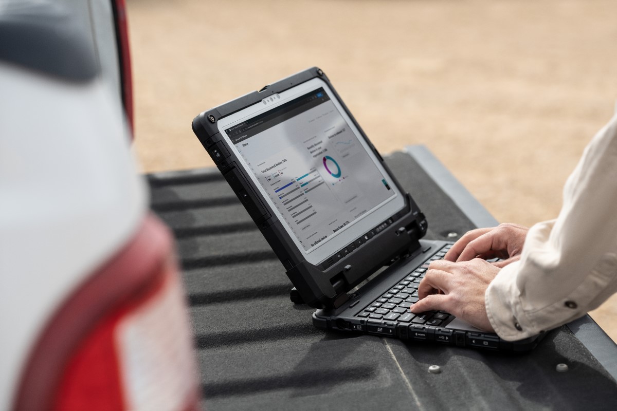 Field engineer using a laptop on truck tailgate to review data after inspection of turbines on a wind farm