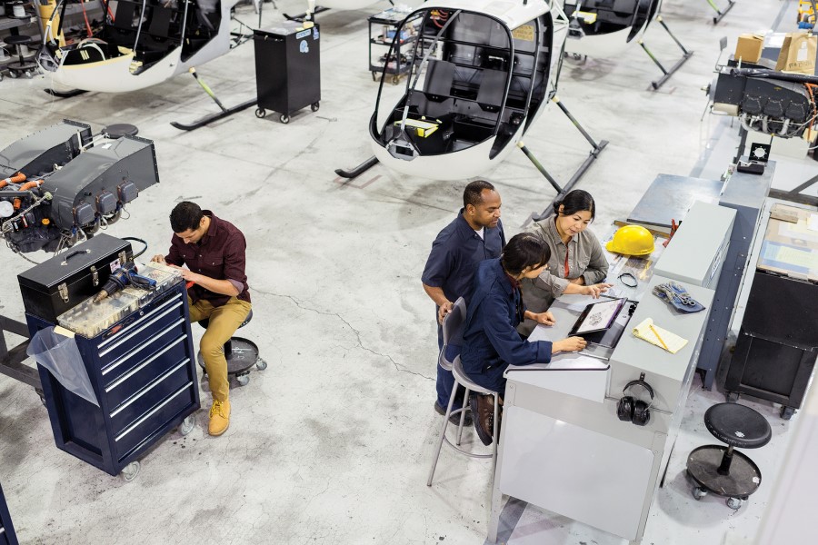 Overhead view of three first line workers on helicopter factory floor at commercial manufacturing plant