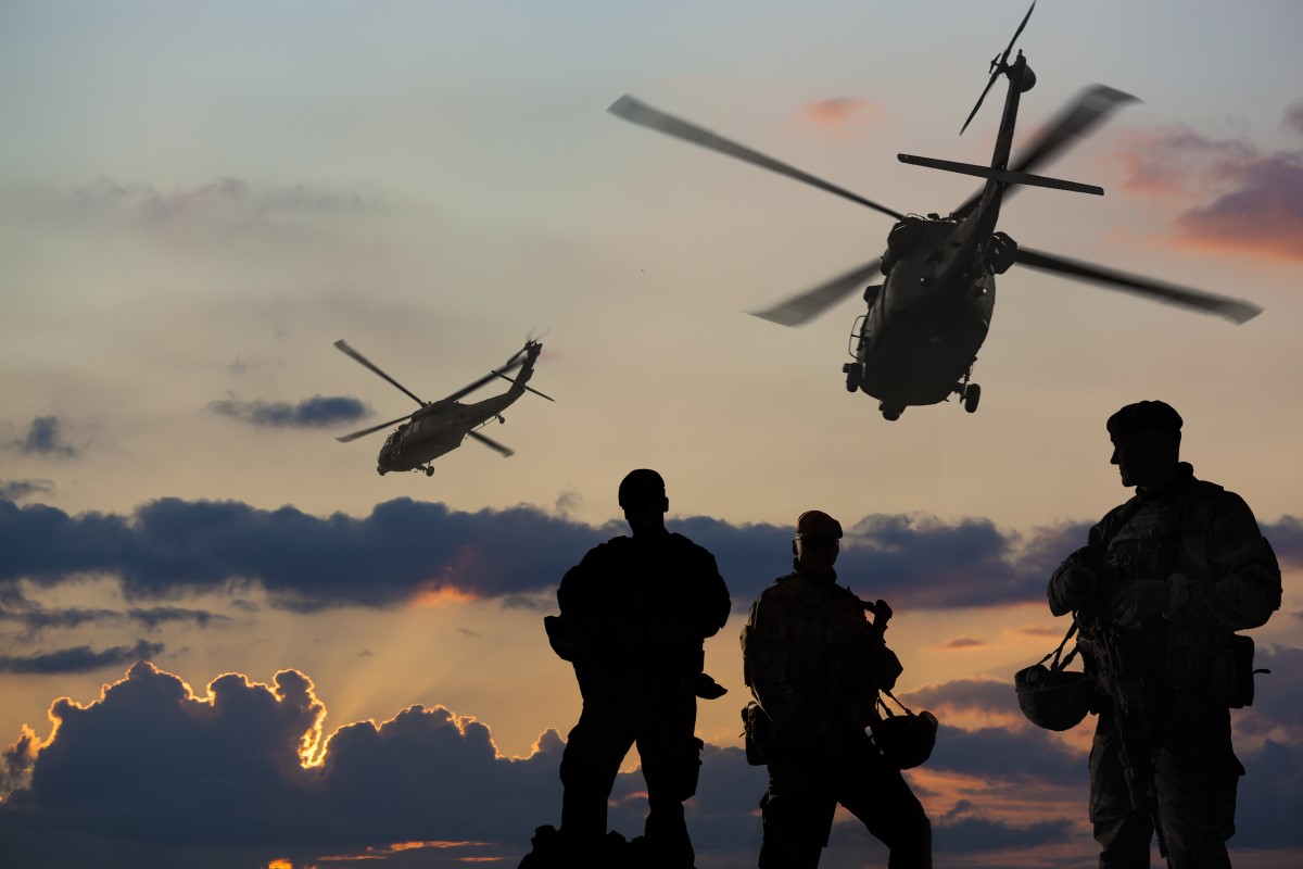 Three marines in the foreground with two helicopters in the background