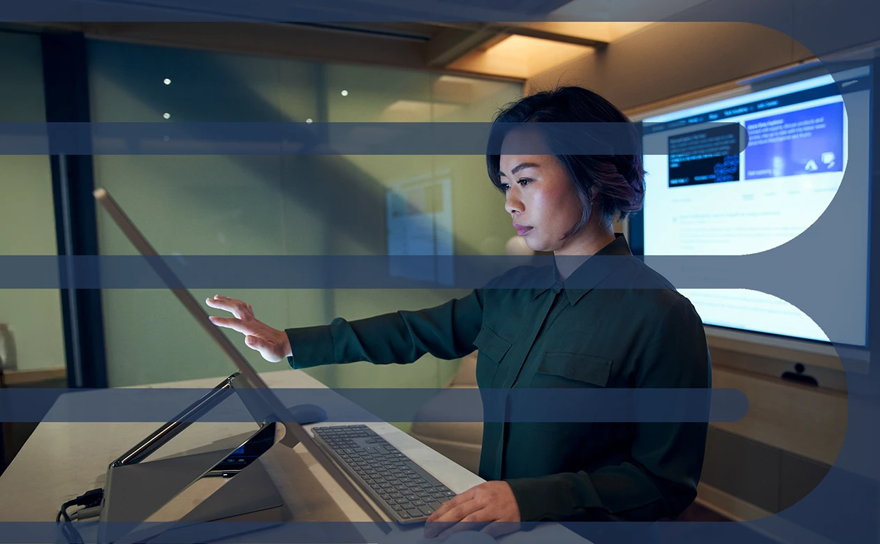 Side profile of a woman wearing a dark shirt in a dim office scrolling or working on a Microsoft Surface Studio