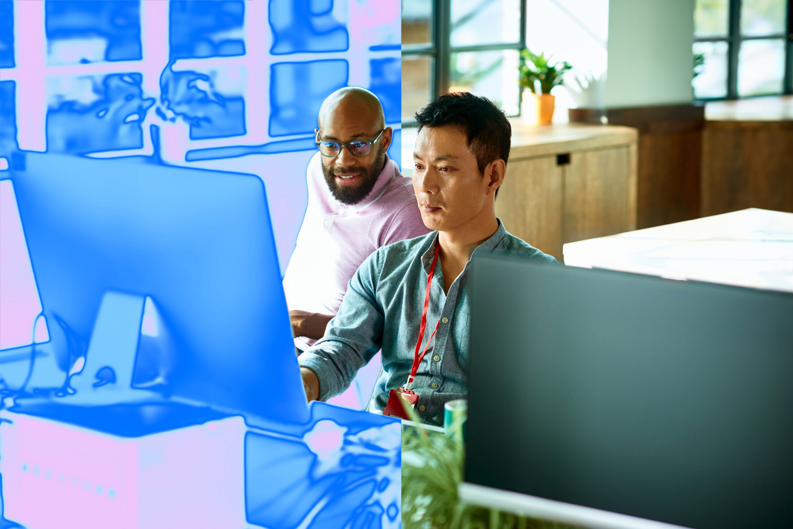 Two men sitting at a desk in front of computer monitor in an office setting with a blue overlay on the image
