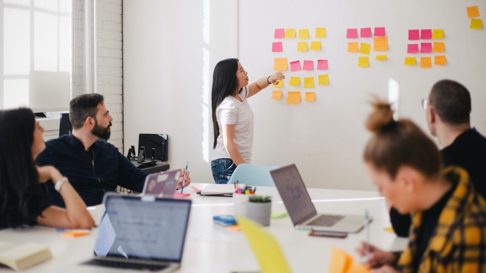 A woman points to sticky notes in a conference room as others look on