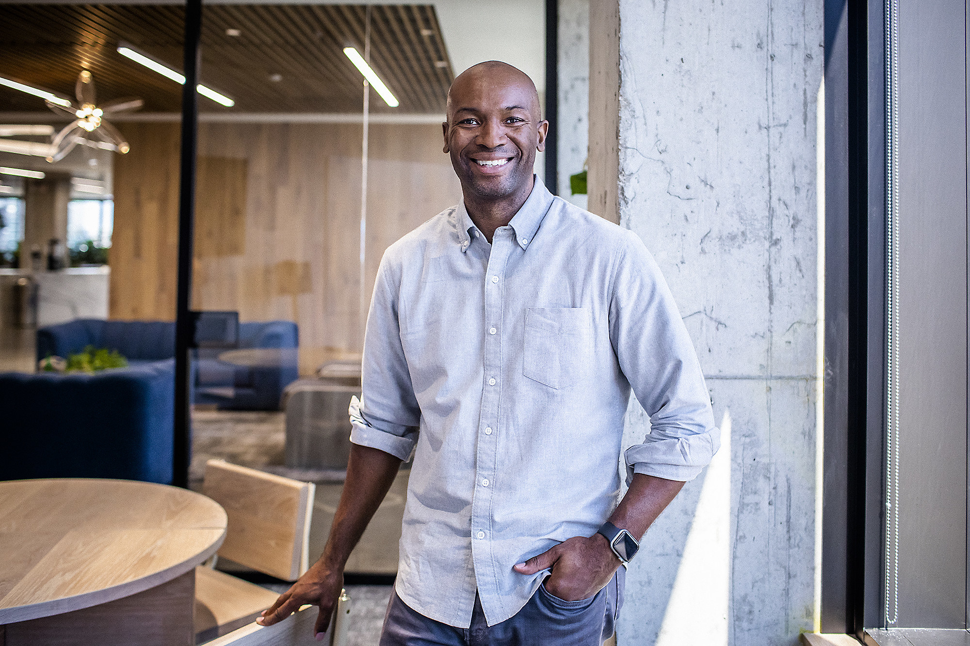 Black man standing and smiling in a office in a blue collared shirt