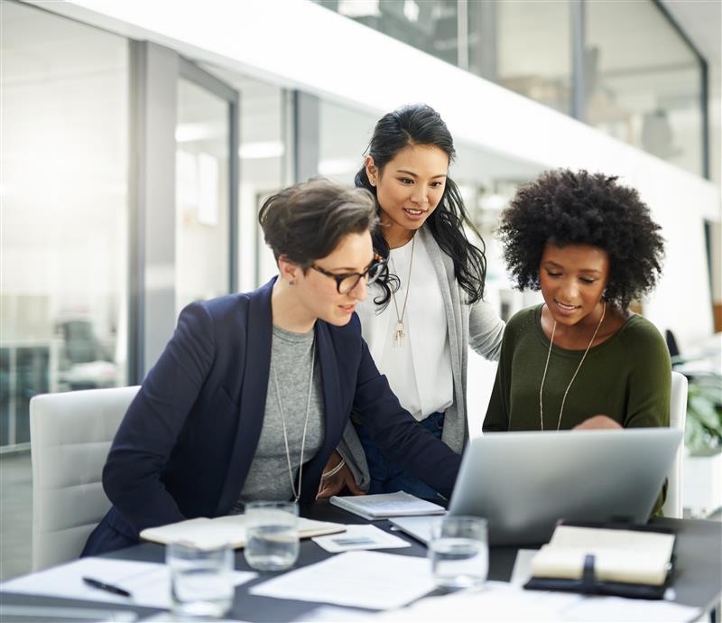 Three women working at a desk with a computer