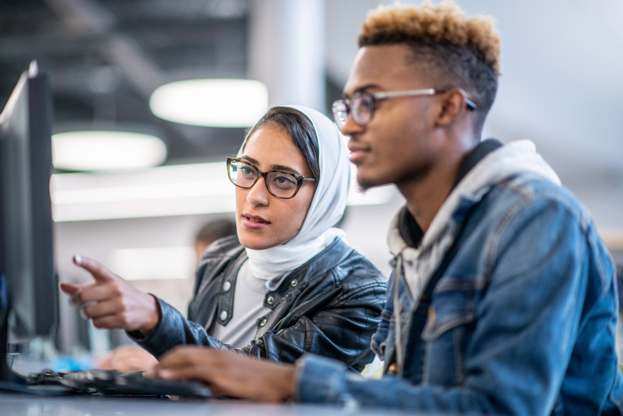 A young female student helps a classmate with a project in the computer lab