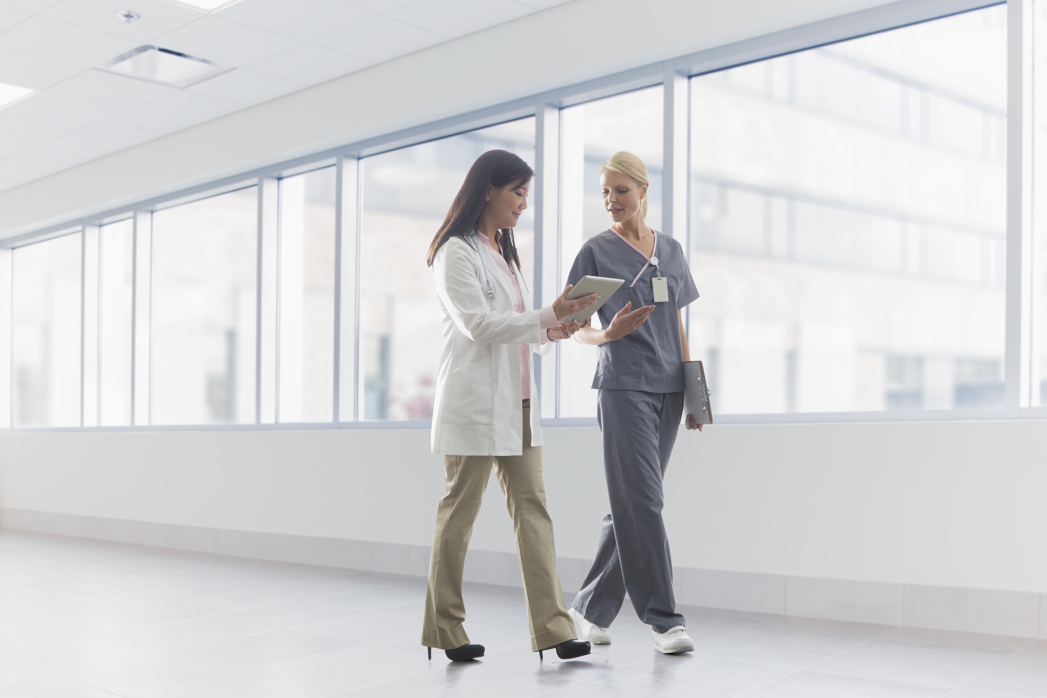 Two doctors walking down a hallway in a hospital looking at a tablet device