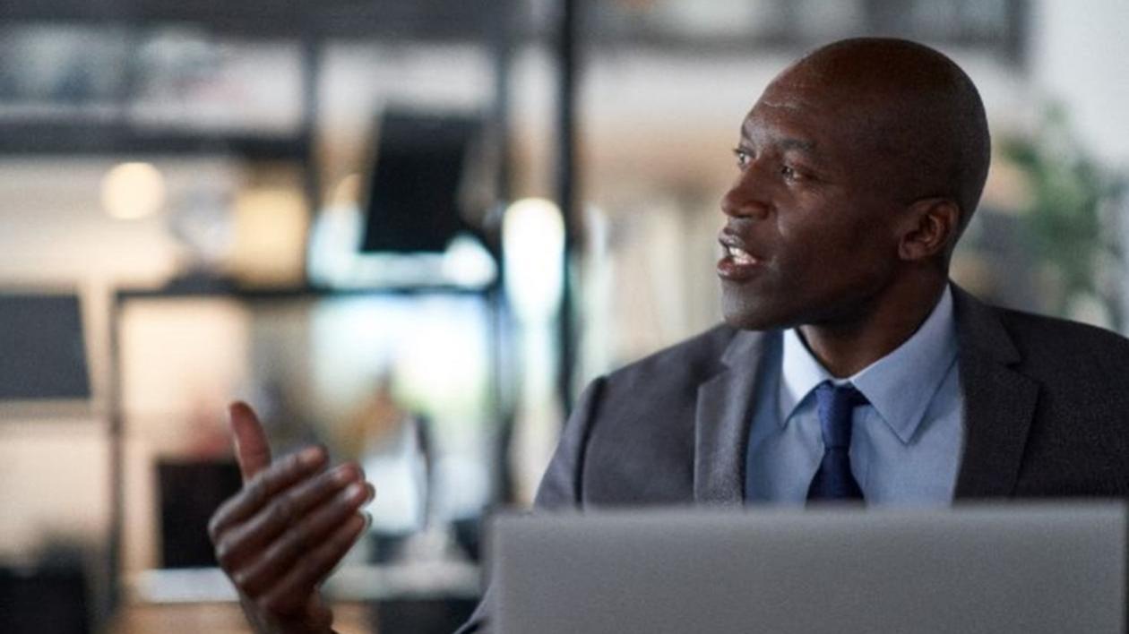 A Chief Technology Officer in a gray suit sits in front of an open silver laptop having a serious discussion