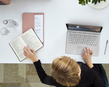 Overhead-visning af en person, der bruger en bærbar computer, mens du også kigger på ord i en ordbog