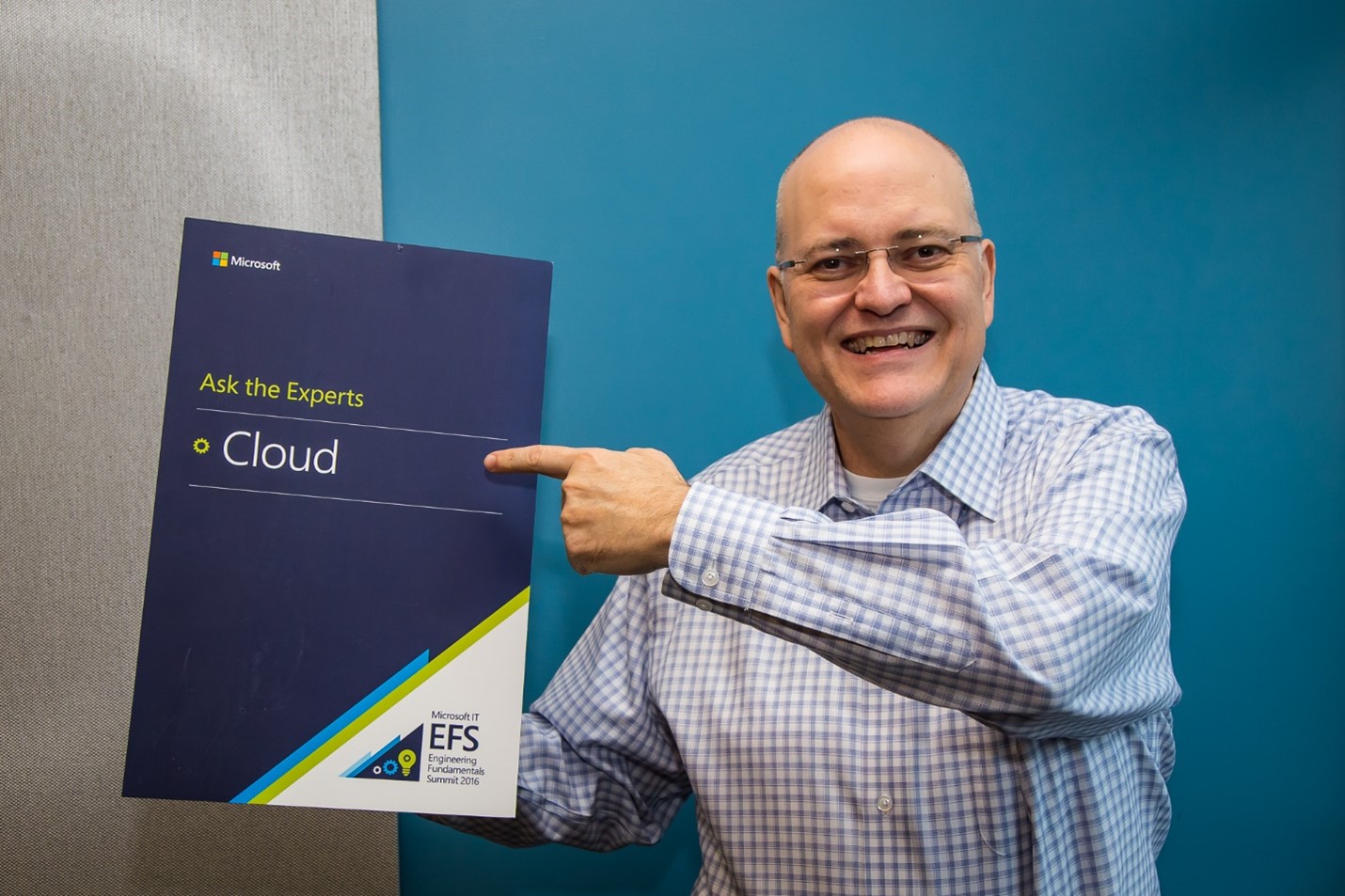 男性が「Ask the Experts Cloud」と書かれたマイクロソフトのポスターを指差している。