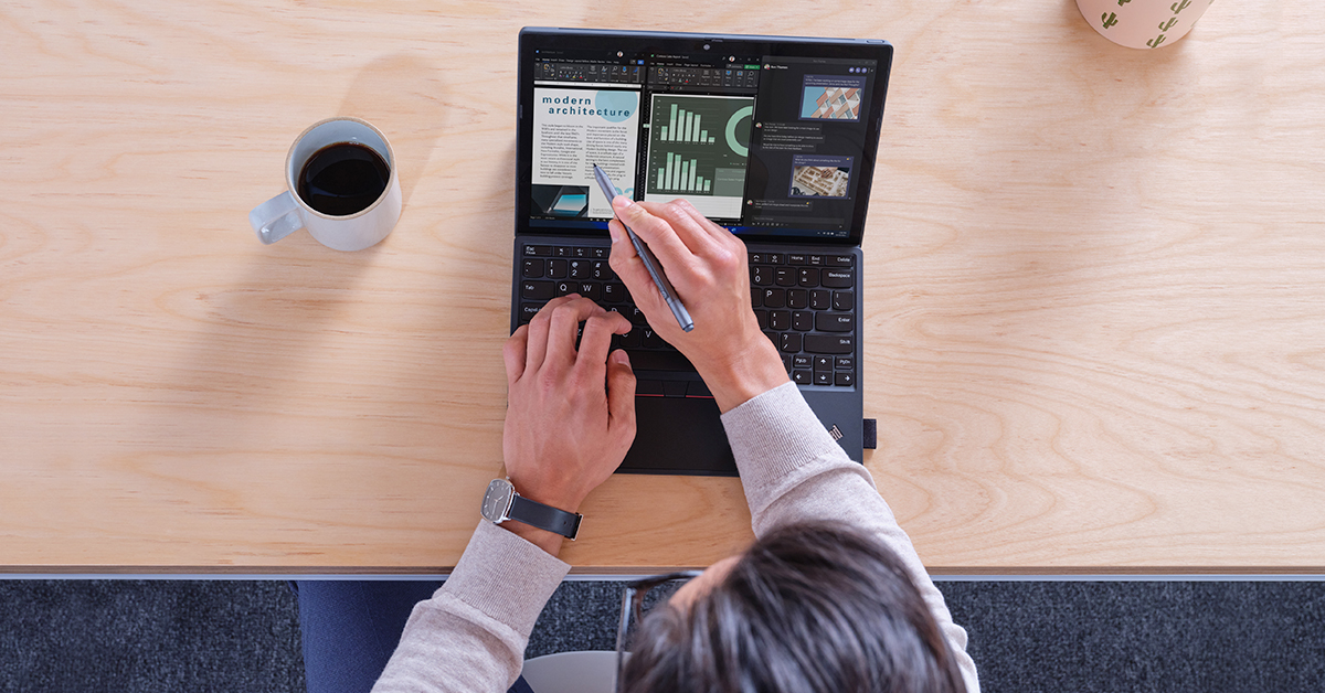 コーヒーが置かれたデスクの上で PC を操作する男性を上から見た様子
