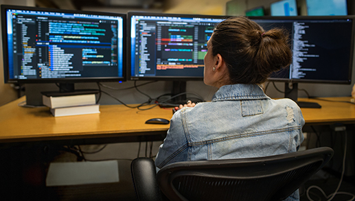 Desenvolvedora codificando seu espaço de trabalho em um escritório empresarial, usando Visual Studio em um conjunto de monitores múltiplos